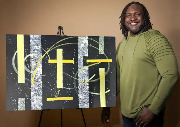 Artist James Sanders stands next to his original abstract painting. The artwork features bold colors and dynamic shapes.
