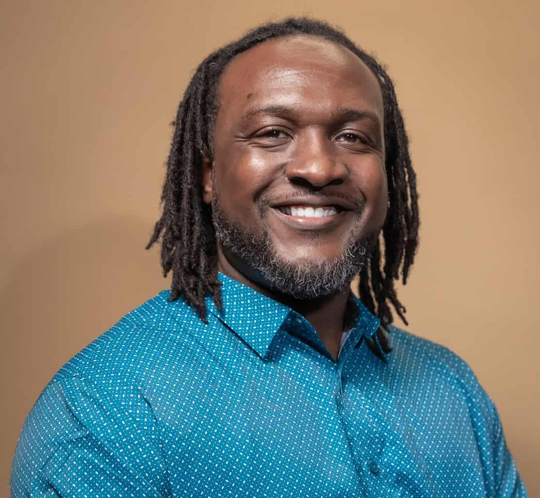 Image of arts James Sanders smiling against a soft brown background wearing a teal shirt