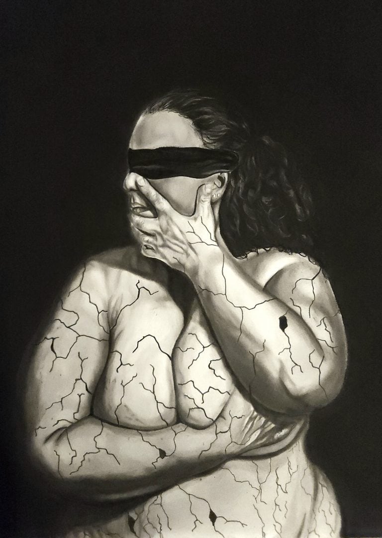 Graphite and charcoal drawing, 'In Pieces pt. 1.' The piece features the torso of a man wearing a blindfold. He crosses his arms to hold himself in a protective gesture, while cracks spiderweb across his skin, rendered with detailed shading to resemble fractured concrete. The monochrome artwork evokes a powerful sense of vulnerability and hidden turmoil.